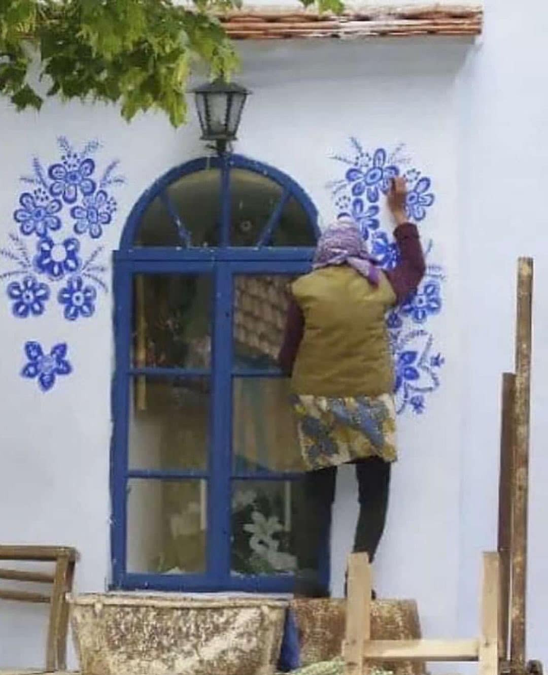 Bà sử dụng màu xanh lam rực rỡ để tạo ra những bông hoa cách điệu, làm nổi bật vẻ đẹp của ngôi làng.