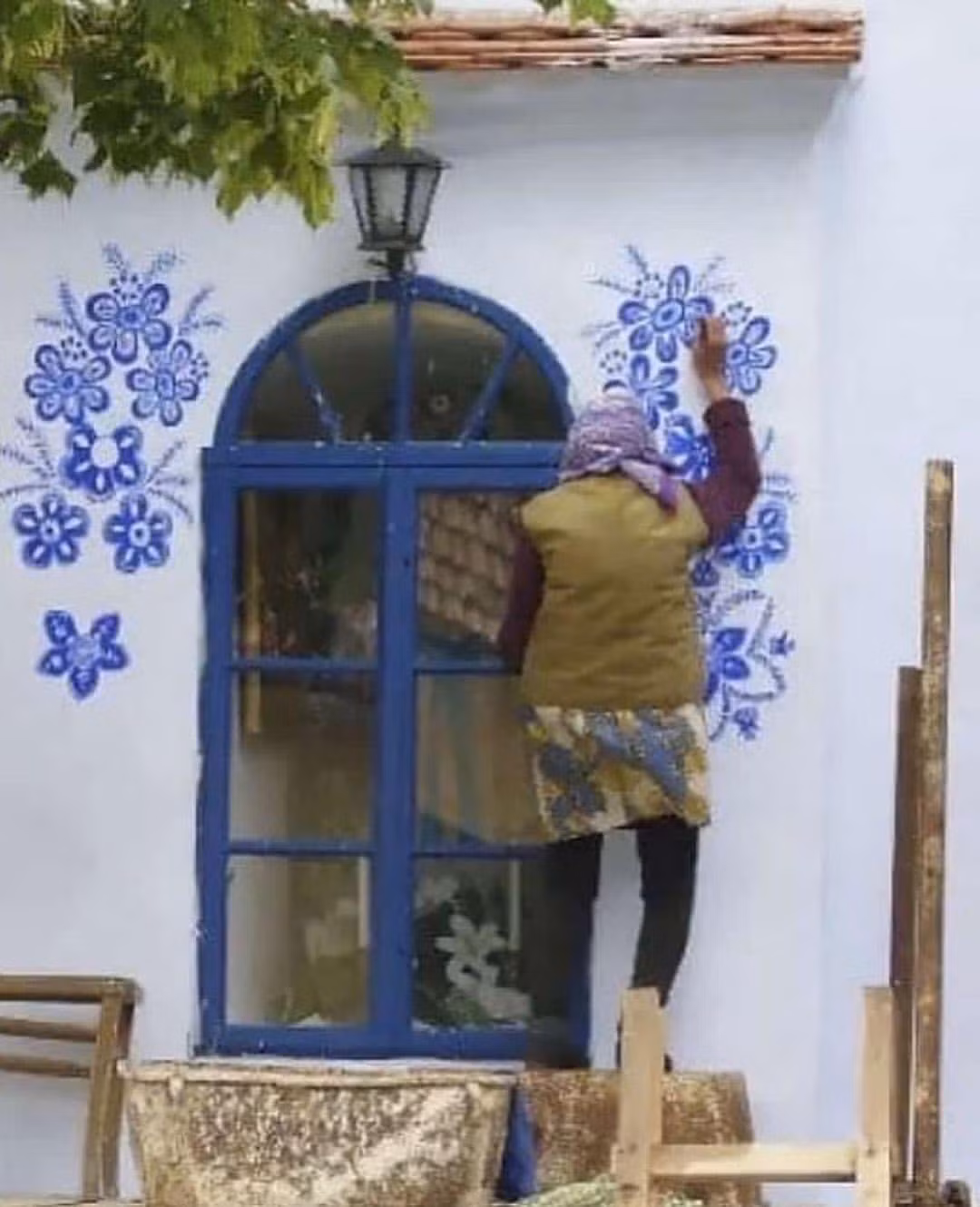 Bà sử dụng màu xanh lam rực rỡ để tạo ra những bông hoa cách điệu, làm nổi bật vẻ đẹp của ngôi làng.