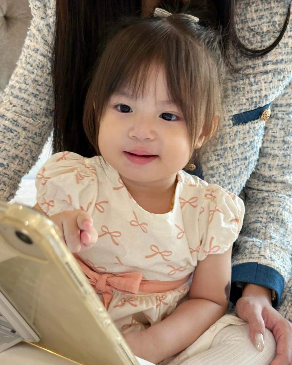 Vẫn gương mặt vuông đáng yêu đấy nhưng cô bé ngoan ngoãn ngồi yên trong lòng mẹ.