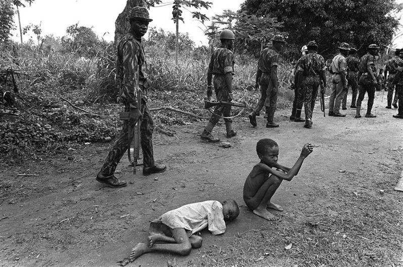 Quân đội Liên bang Nigeria hành quân dọc theo một con đường gần biên giới với Biafra - một nhà nước ly khai đã chiến đấu trong cuộc chiến giành độc lập từ năm 1967-1970. Bên lề đường là những đứa trẻ suy kiệt vì nạn đói. Ảnh chụp ngày 13/10/1968. Ảnh: The Atlantic.