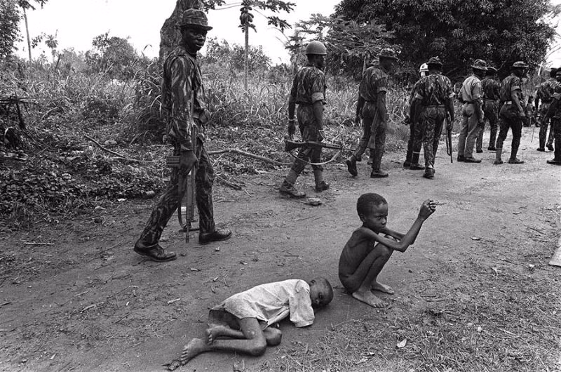 Quân đội Liên bang Nigeria hành quân dọc theo một con đường gần biên giới với Biafra - một nhà nước ly khai đã chiến đấu trong cuộc chiến giành độc lập từ năm 1967-1970. Bên lề đường là những đứa trẻ suy kiệt vì nạn đói. Ảnh chụp ngày 13/10/1968. Ảnh: The Atlantic.