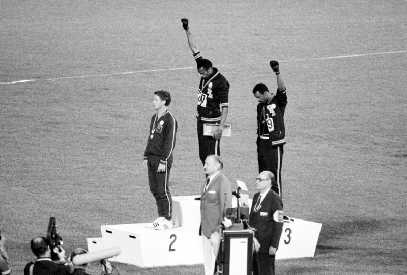 Hai vận động viên Mỹ Tommie Smith và John Carlos giành huy chương vàng và đồng trong bộ môn chạy 200 mét tại Olympic 1968. Họ đã cúi đầu, giơ tay đeo găng đen, từ chối chào cờ Mỹ và hát quốc ca để biểu lộ sự phản kháng với nạn phân biệt chủng tộc ở Mỹ. Ảnh: The Atlantic.
