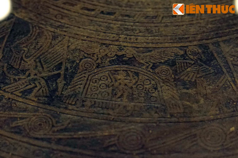 Nhóm thứ hai có một nhà sàn cầu mùa mái vòm, trên nóc có một đôi chim đuôi dài, chim bên trái đứng trên trụ mái nhà, chim bên phải đứng trên nóc nhà, đang mớm cho nhau, giữa nhà là hình người đang đứng làm lễ.