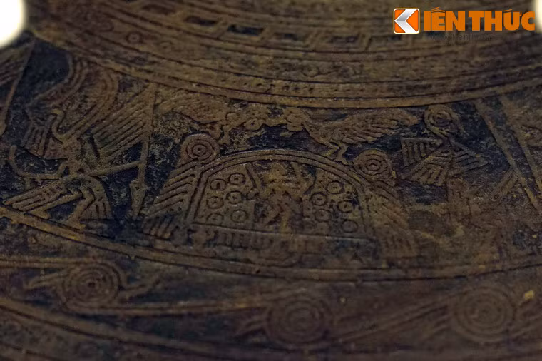 Nhóm thứ hai có một nhà sàn cầu mùa mái vòm, trên nóc có một đôi chim đuôi dài, chim bên trái đứng trên trụ mái nhà, chim bên phải đứng trên nóc nhà, đang mớm cho nhau, giữa nhà là hình người đang đứng làm lễ.