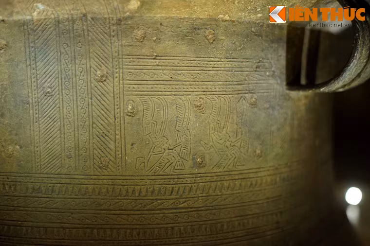 Thân trống có 7 vành hoa văn. Vành số 1 là hoa văn chấm giữa, hoa văn gạch chéo vào vòng tròn tiếp tuyến, chia làm 6 ô theo chiều dọc, trong mội ô có hai người hóa trang lông chim, chuyển động từ trái sang phải, tay cầm rìu chiến và tay cầm mộc hình đầu chim.