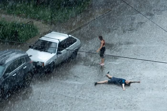 Sau cái nóng 40 độ C, trời cuối cùng cũng mưa. Bức ảnh chụp một người đàn ông nằm trên đường dưới trời mưa để giải nhiệt vào mùa hè.