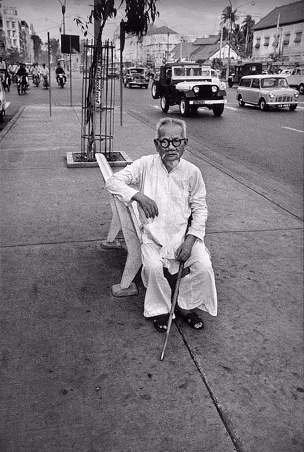 Một cụ ông ngồi nghỉ trên ghế đá vỉa hè.