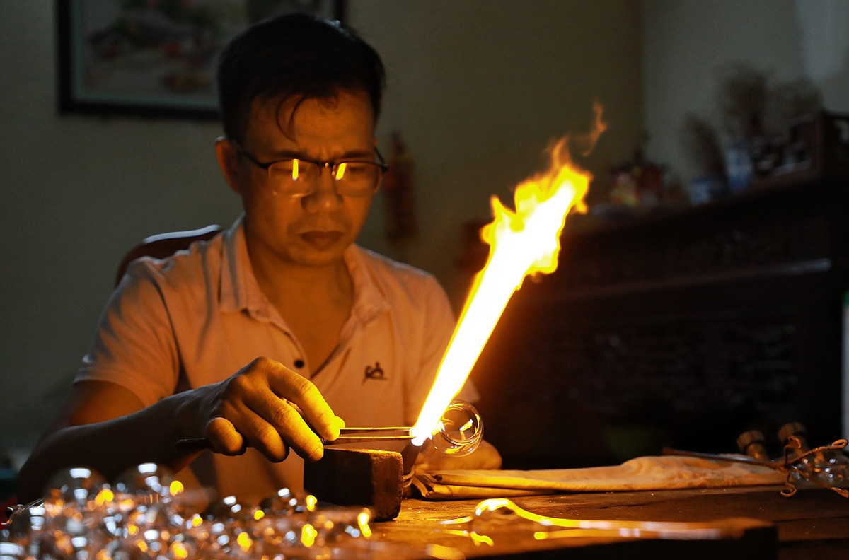 Thời tiết Hà Nội đang trong những ngày nắng nóng gay gắt, nhưng trong xưởng chế tác thuỷ tinh của ông Đặng Văn Thạo (46 tuổi, ở xã Thống Nhất) vẫn luôn đỏ rực ngọn lửa đèn khò với nhiệt độ rất cao trước mặt để làm ra những sản phẩm truyền thống.