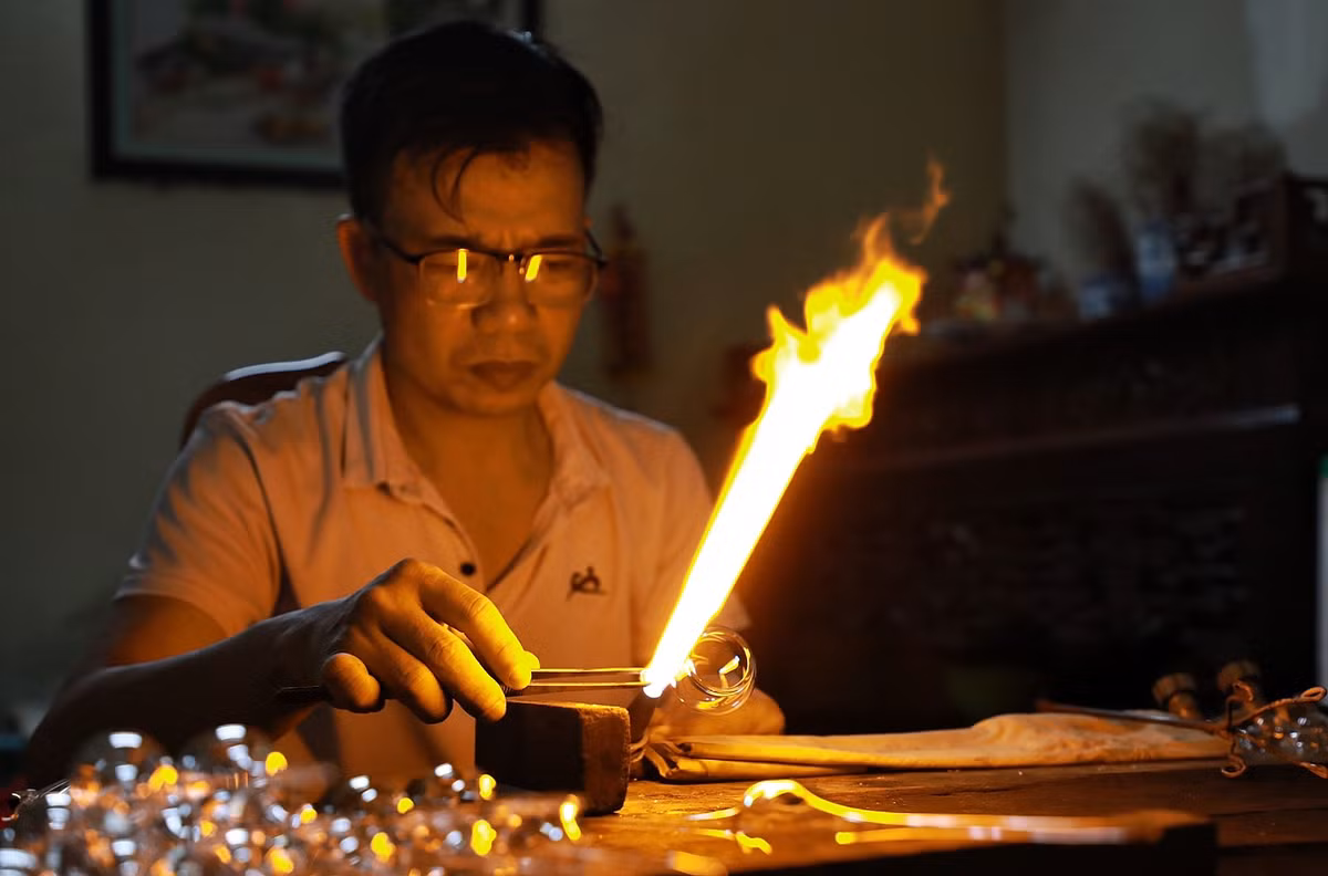Thời tiết Hà Nội đang trong những ngày nắng nóng gay gắt, nhưng trong xưởng chế tác thuỷ tinh của ông Đặng Văn Thạo (46 tuổi, ở xã Thống Nhất) vẫn luôn đỏ rực ngọn lửa đèn khò với nhiệt độ rất cao trước mặt để làm ra những sản phẩm truyền thống.