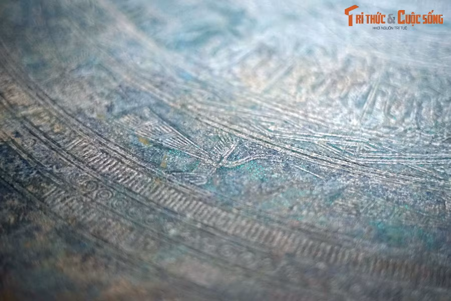 Cảnh sinh hoạt được thể hiện trên mặt trống qua hình tượng người hóa trang xen kẽ bốn ngôi nhà sàn mái cong, mái rủ. Một đường vành trang trí hình chim lạc xoay ngược chiều kim đồng hồ.