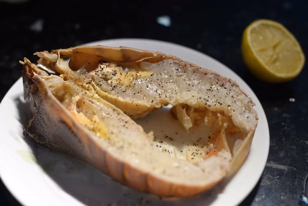 Sau khi rửa sạch, dùng kéo cắt đôi tôm mũ ni. Thoa đều hỗn hợp gồm bơ, nước cốt chanh, tỏi, hạt tiêu, ớt lên mặt tôm. Ảnh: Healthplus.