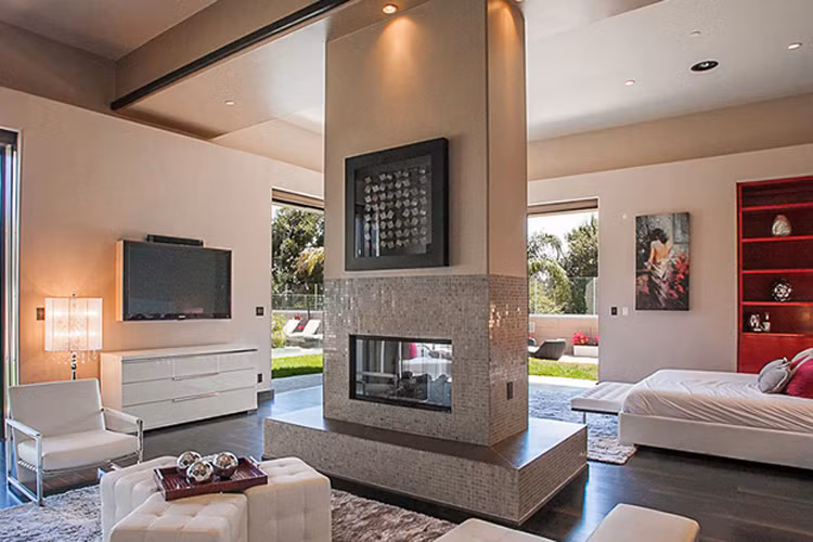 Lò sưởi ở giữa giúp tạo không gian tách biệt giường ngủ với bàn ghế xem tivi trong phòng ngủ. 