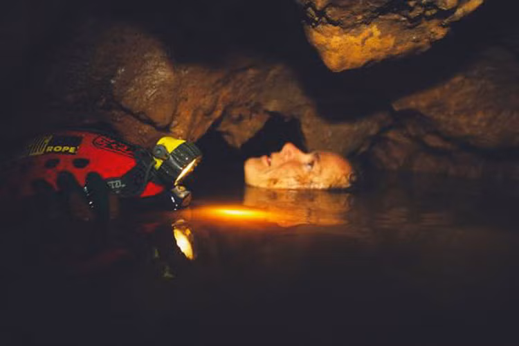 Người phụ nữ cầm mũ bảo hiểm và bơi qua khe hẹp trong một hang động ở Thái Lan.