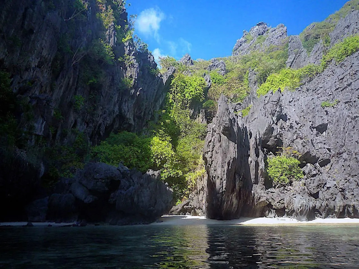 Khi đến gần hòn đảo Dilumacad, mọi người sẽ có thể chiêm ngưỡng những vách đá cao sừng sững, khu rừng nhiệt đới rậm rạp với nhiều loại cây. Phần phía "đuôi trực thăng" là bãi biển cát trắng mịn, nước biển xanh tuyệt đẹp. Ảnh: tikigo.
