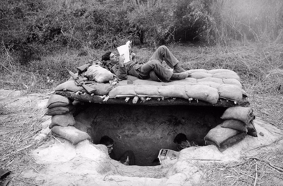 Một người lính đọc báo trên một căn hầm giữa rừng khu vực biên giới Việt Nam - Campuchia, tháng 11/1966. Ảnh: Horst Faas/ AP