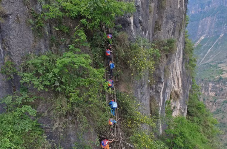 Ảnh các em học sinh nhỏ tuổi Trung Quốc leo dây thang nằm bên vách đá. Để đảm bảo an toàn, người dân trong làng cử các nam giới khỏe mạnh để giúp 15 em vượt qua đoạn đường nguy hiểm này.