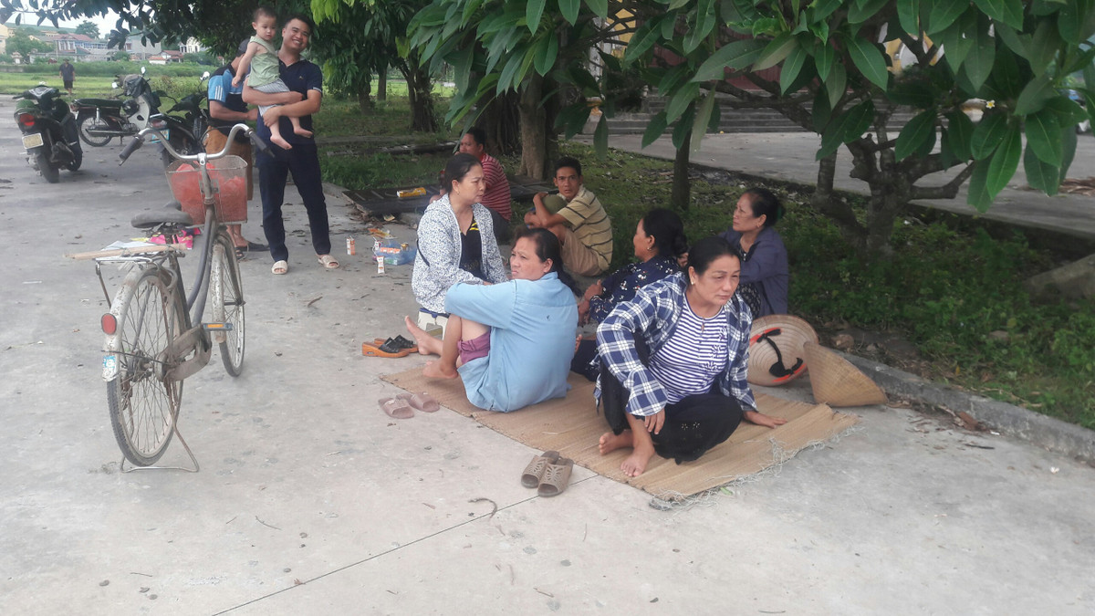 Ghi nhận điểm tập trung chặn xe rác tại thôn Liên Xuân cho thấy nhiều người dân dải chiếu ngồi tập chung tại các gốc cây.