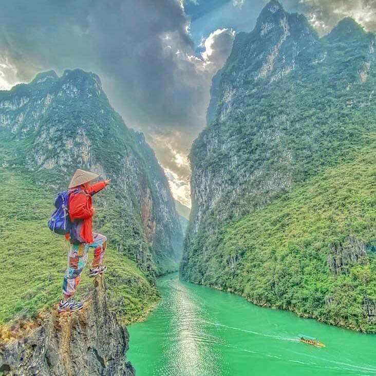 Từ trên cao nhìn xuống, dưới chân đèo là dòng sông Nho Quế xanh biếc uốn lượn, phía xa xa là ruộng hoa tam giác mạch phớt hồng dịu dàng, không gian vốn hùng vĩ lại thêm vẻ trữ tình. Ảnh: TINTIN ADVS