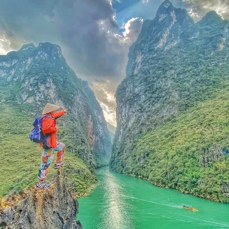 Từ trên cao nhìn xuống, dưới chân đèo là dòng sông Nho Quế xanh biếc uốn lượn, phía xa xa là ruộng hoa tam giác mạch phớt hồng dịu dàng, không gian vốn hùng vĩ lại thêm vẻ trữ tình. Ảnh: TINTIN ADVS