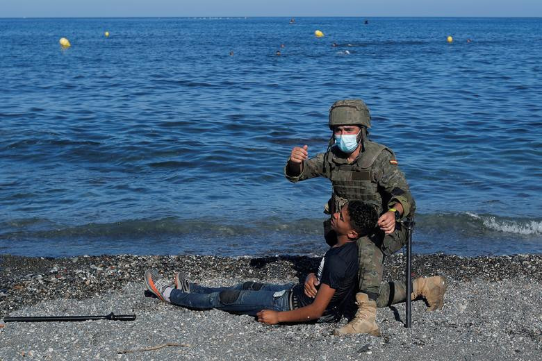 Binh sĩ Tây Ban Nha hỗ trợ một cư dân Ma-rốc bị ngất trên bãi biển El Tarajal, gần hàng rào biên giới Tây Ban Nha - Ma-rốc, ở Ceuta ngày 18/5.