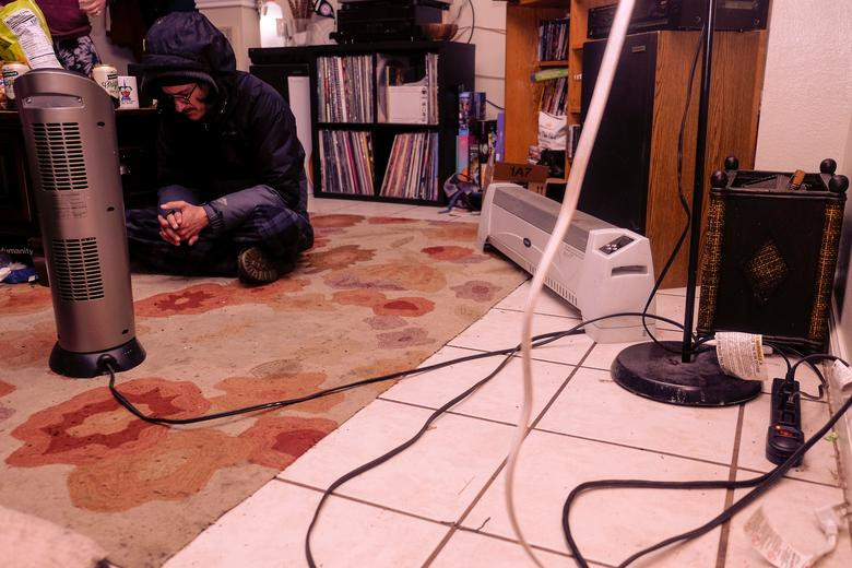 Scott Bruffy ngồi gần máy sưởi chạy bằng máy phát điện trong nhà ở San Marcos hôm 16/2.