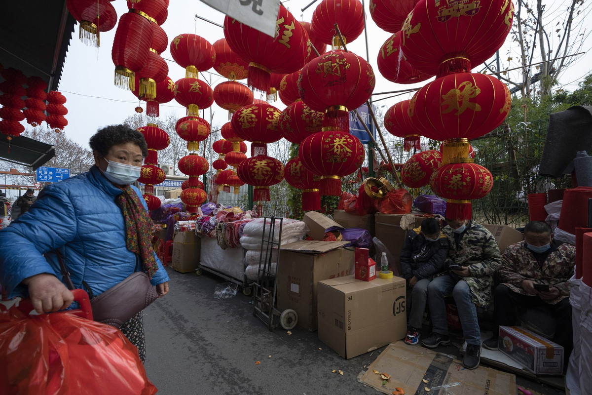 Một phụ nữ đeo khẩu trang phòng COVID-19 khi đi qua những chiếc đèn lồng được treo bên ngoài một cửa hàng trước thềm Tết Nguyên đán 2021, tại Vũ Hán ngày 26/1.