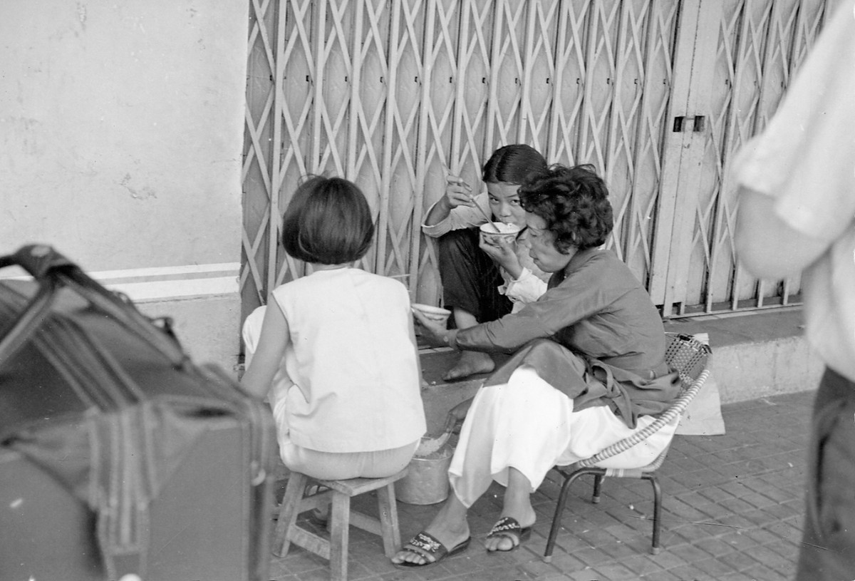 Bữa ăn trên vỉa hè của người phụ nữ bán hàng rong cùng hai em nhỏ. Ảnh: Vietnam Center and Archive.