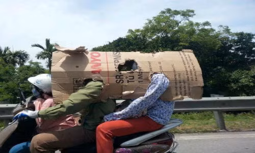 Những tờ bìa cứng được tận dụng để làm phương tiện tránh nóng hữu hiệu. Tuy nhiên, việc chở đông người và mang vật cồng kềnh như thế này sẽ rất nguy hiểm. Ảnh: Nhạt Nhòa.