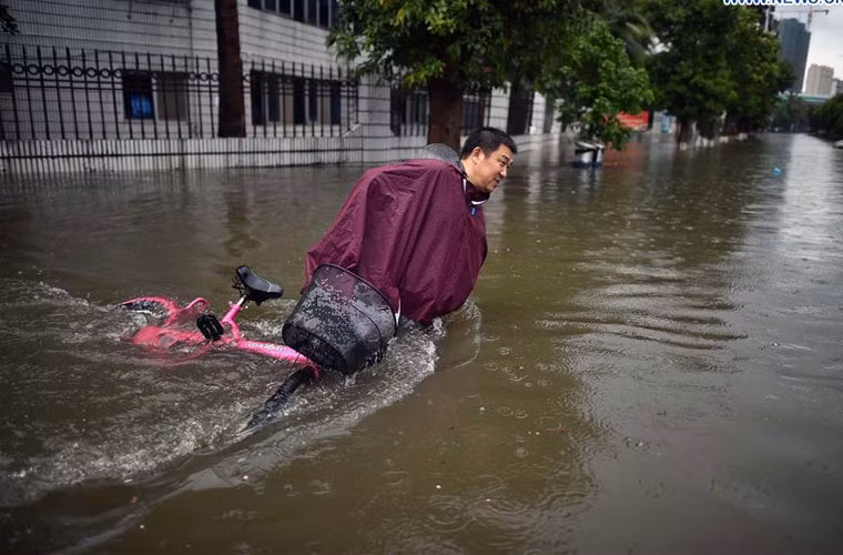 Người đàn ông cố gắng dắt xe đap điện đi qua đoạn đường ngập úng ở Hải Khẩu.