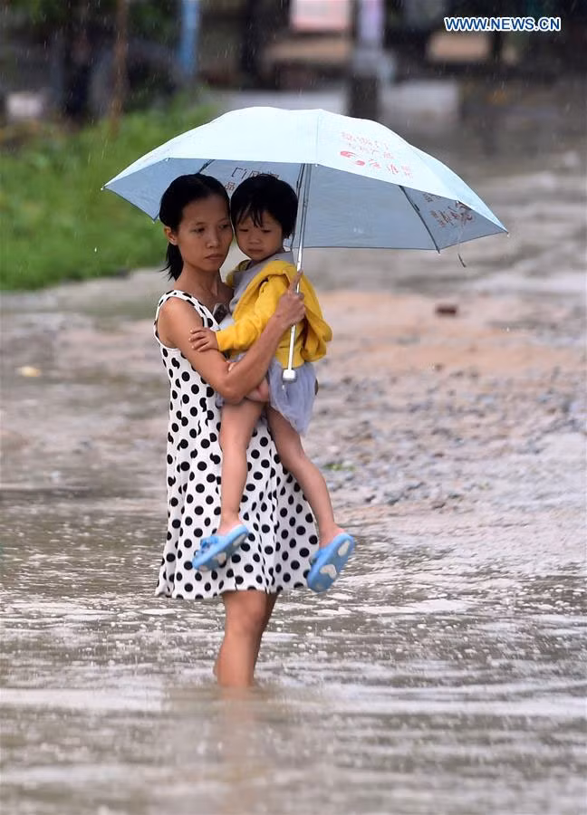 Người phụ nữ ôm chặt con trong lúc lội qua dòng nước do bão Dianmu gây ra ở thị trấn Lincheng, huyện Lingao, tỉnh Hải Nam.