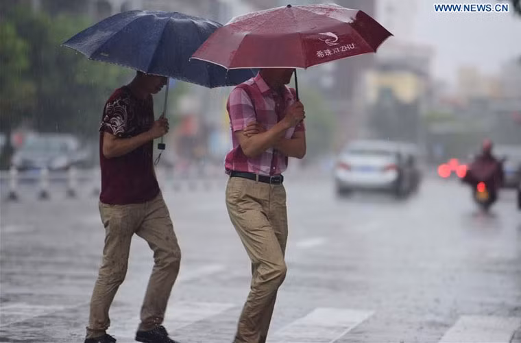 Người dân cầm ô đi sang đường trong lúc trời mưa to do ảnh hưởng của bão Dianmu ở thành phố Quỳnh Hải, tỉnh Hải Nam ngày 18/8.