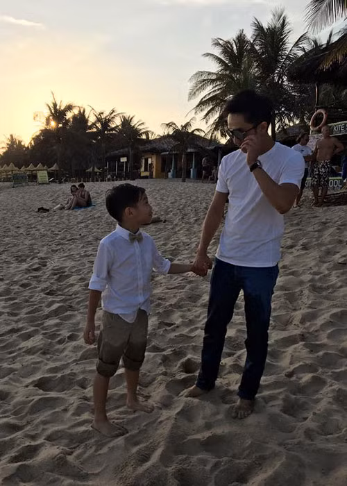 Cường Đô-la và con trai đều diện áo trắng và nắm tay nhau vô cùng tình cảm khi dạo chơi trên bờ biển. 