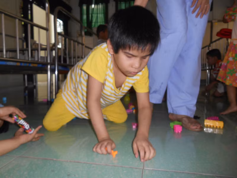 Bé H. bị mù, liệt chân đang bò trên sàn nhà.