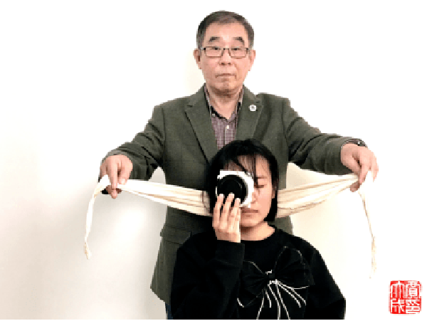 Gấp một chiếc khăn tam giác thành một dải có chiều dài đủ quấn quanh mắt bệnh nhân. Đặt điểm giữa của dải khăn ở chính gáy.