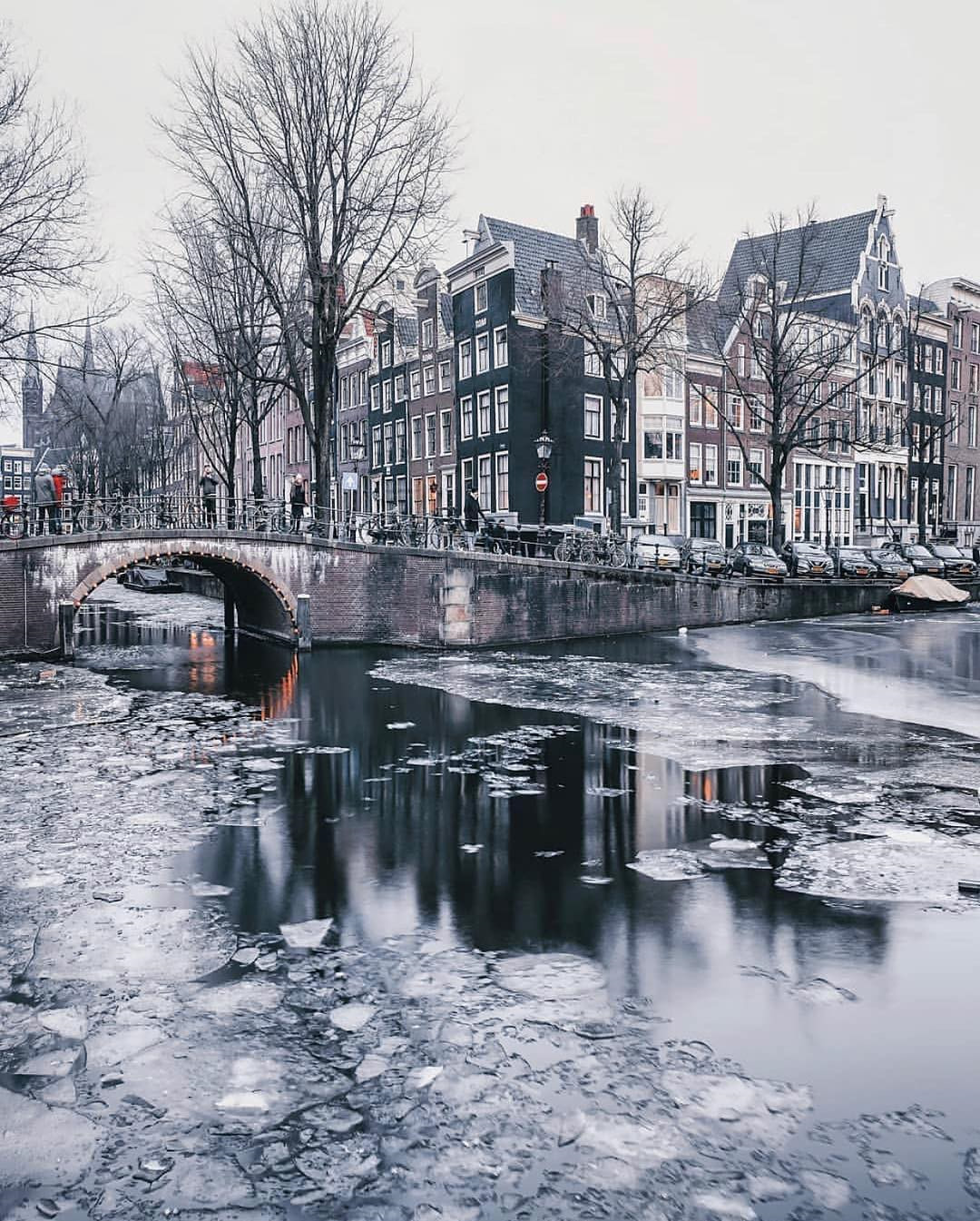 Amsterdam, Hà Lan: Vào mùa đông, tuyết phủ trắng các con kênh dọc thành phố Amsterdam tạo khung cảnh thần tiên cho miền đất sản sinh ra các câu truyện cổ tích. Các sự kiện mùa đông được tổ chức rất nhiều ở thủ đô Hà Lan như sân trượt băng, đèn nhiều màu thắp sáng trung tâm thành phố, diễu hành đường phố, nhạc kịch và các chương trình văn hóa đặc sắc. Thăm thú Amsterdam vào mùa đông, du khách không khó để bắt gặp khung cảnh hàng dài những chiếc xe đạp dựng quanh thành cầu bị tuyết phủ kín, tạo nên nét đặc trưng riêng cho thành phố thơ mộng. Ảnh: Magictiron, Een_wasbeer.