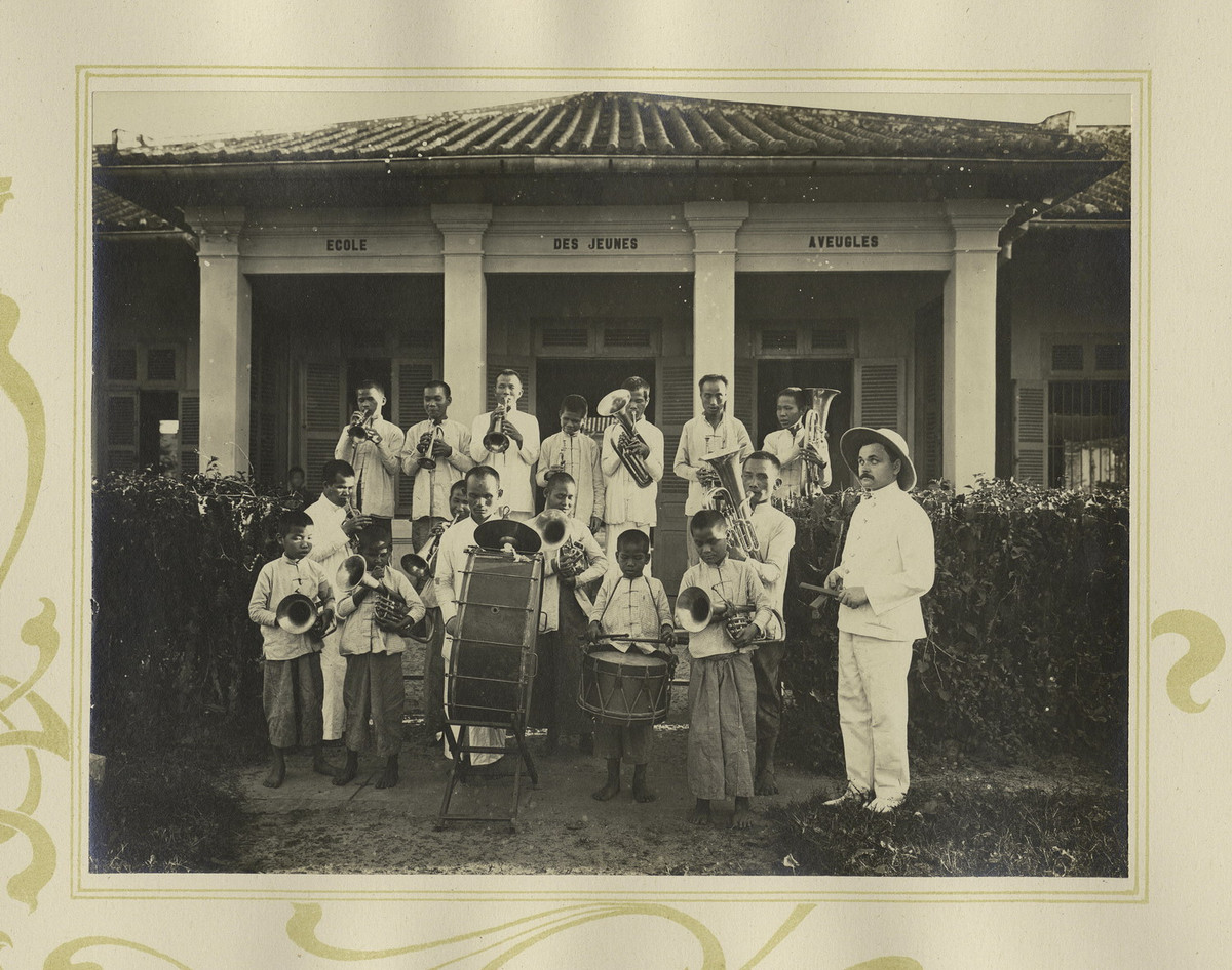 Một ban nhạc kèn đồng gồm những người khiếm thị thuôc hiệp hội bảo vệ người mù Nguyễn Văn Chi ở Chợ Lớn. Mặt tường ở tòa nhà phía sau có chữ "Trường học cho người khiếm thị trẻ".