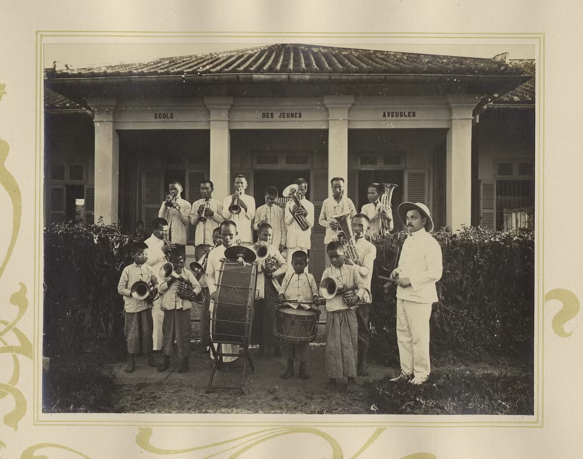 Một ban nhạc kèn đồng gồm những người khiếm thị thuôc hiệp hội bảo vệ người mù Nguyễn Văn Chi ở Chợ Lớn. Mặt tường ở tòa nhà phía sau có chữ "Trường học cho người khiếm thị trẻ".