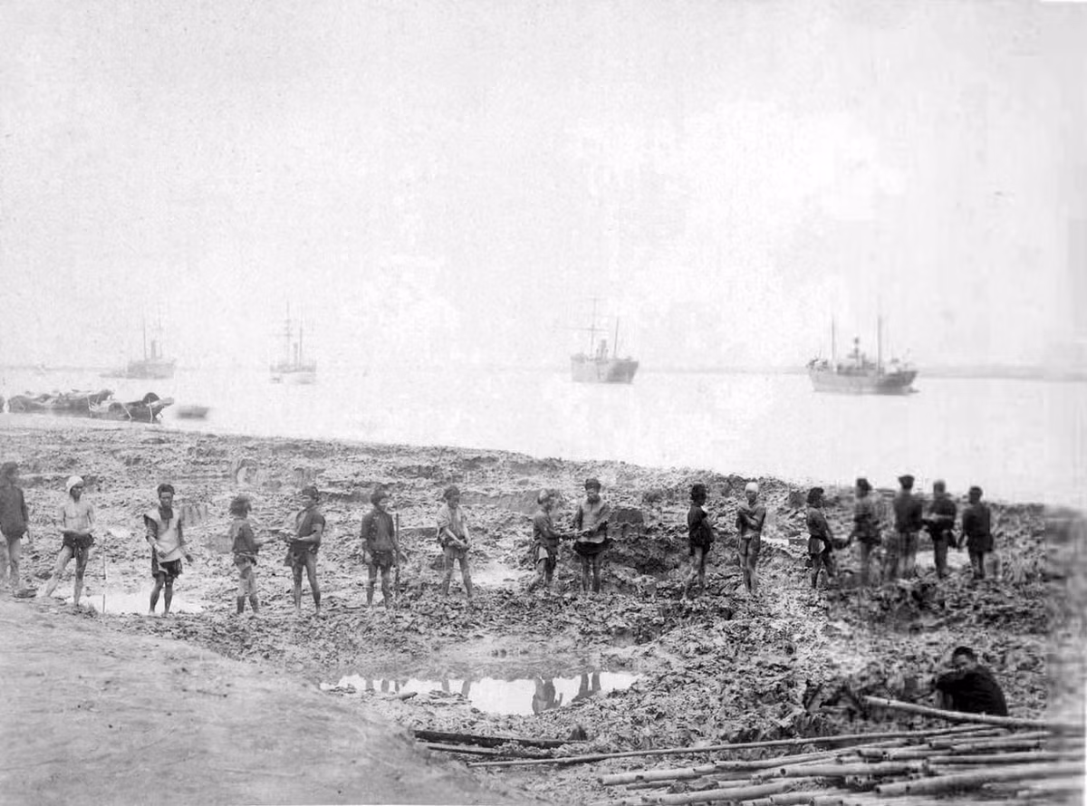 Người lao động bản xứ chuyền tay nhau những tảng bùn khi xây một cảng sông ở Hải Phòng. Phía xa là các con tàu của hãng các tàu của hãng Messageries Maritimes.