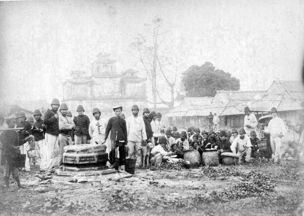 Những người Pháp đứng bên một giếng nước phía sau Hậu lâu, trong thành Hà Nội. Một chợ cóc nhỏ của người địa phương họp cạnh đó.