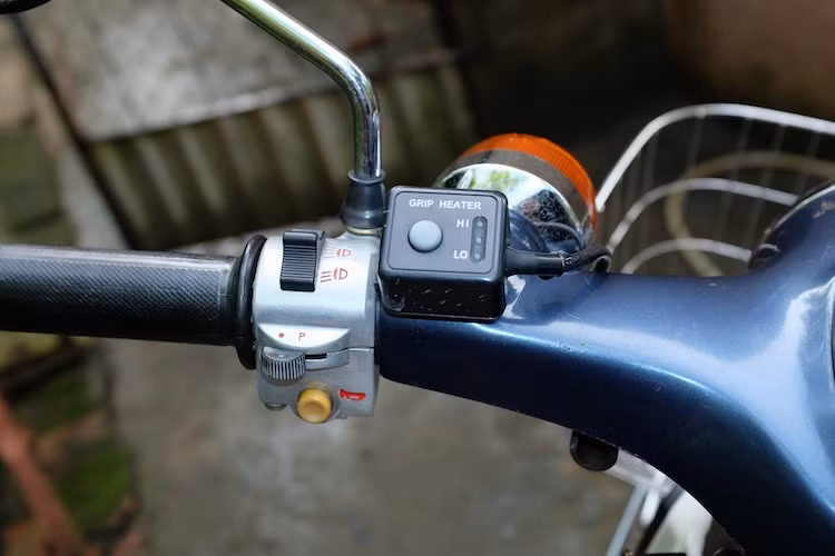 Chi tiết độc đáo đầu tiên trên chiếc xe đó là nó đã được trang bị bộ sưởi tay lái - một phụ kiện "cực độc" của Super Cub tại Nhật - nơi có khí hậu lạnh vào mùa đông. Bộ sưởi tay lái chính hãng Honda này có 2 cấp độ nhiệt cao-thấp, phù hợp với từng điều kiện thời tiết khác nhau.