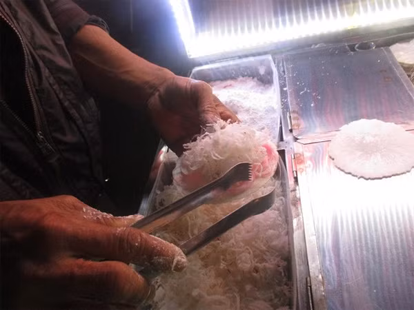 Người chủ bán hàng cho biết, nguyên liệu chính tạo nên loại kẹo này là những sợi chỉ màu hồng làm từ các loại bột kết hợp với dừa khô bào sợi. Tất cả được cuốn trong chiếc bánh đa mỏng. Khi ăn vị khá giống với bò bía ngoài Bắc