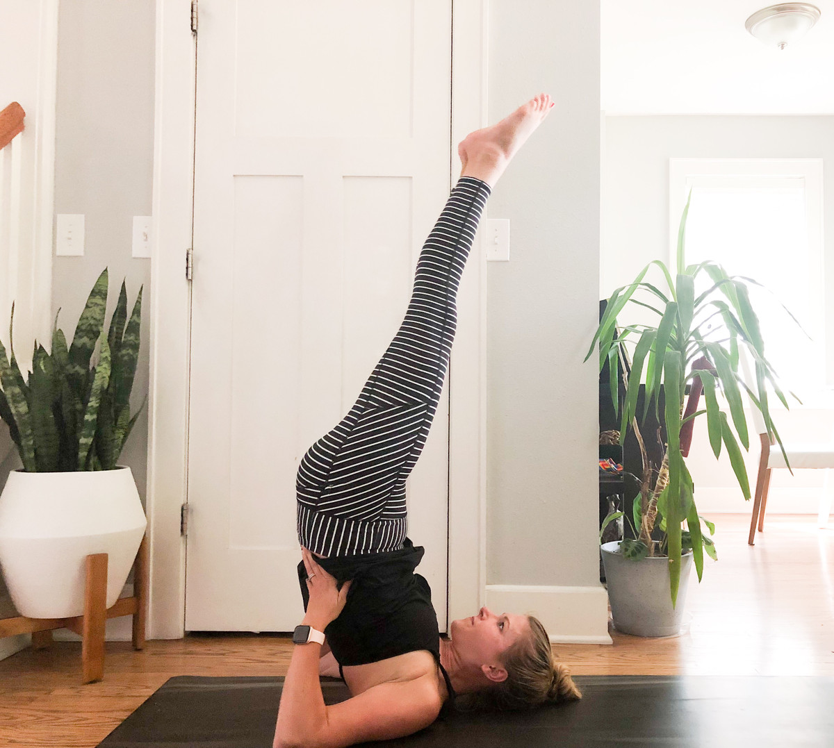 Tiếp theo, bạn thở ra, duỗi thẳng chân rồi dồn trọng lượng xuống hai vai còn hai tay đặt chỗ eo để thăng bằng. Ảnh: cblisslifestyle.