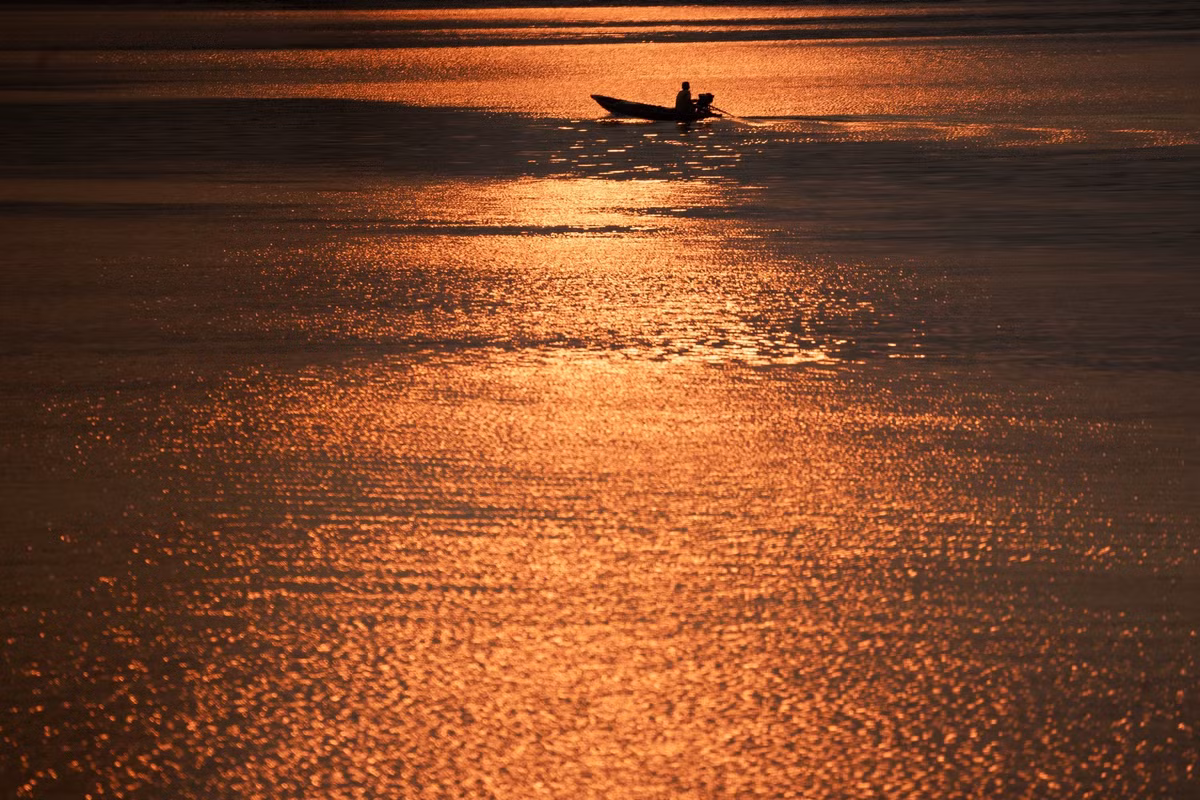 Dòng sông lững lờ trôi, mang theo sắc đỏ cam của hoàng hôn, phản chiếu bóng dáng những con thuyền nhỏ chầm chậm xuôi dòng. Ảnh Kelvin Long