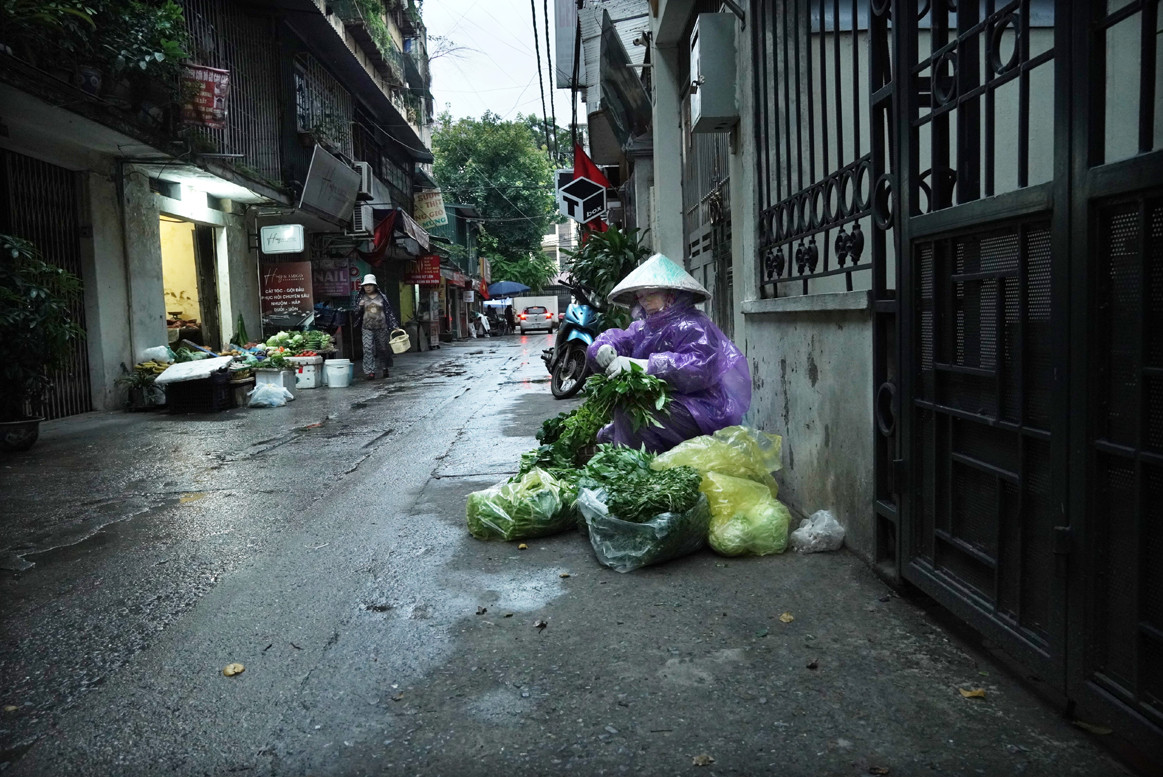 Người bán rau đầu ngõ thu mình trong chiếc áo mưa chống rét.