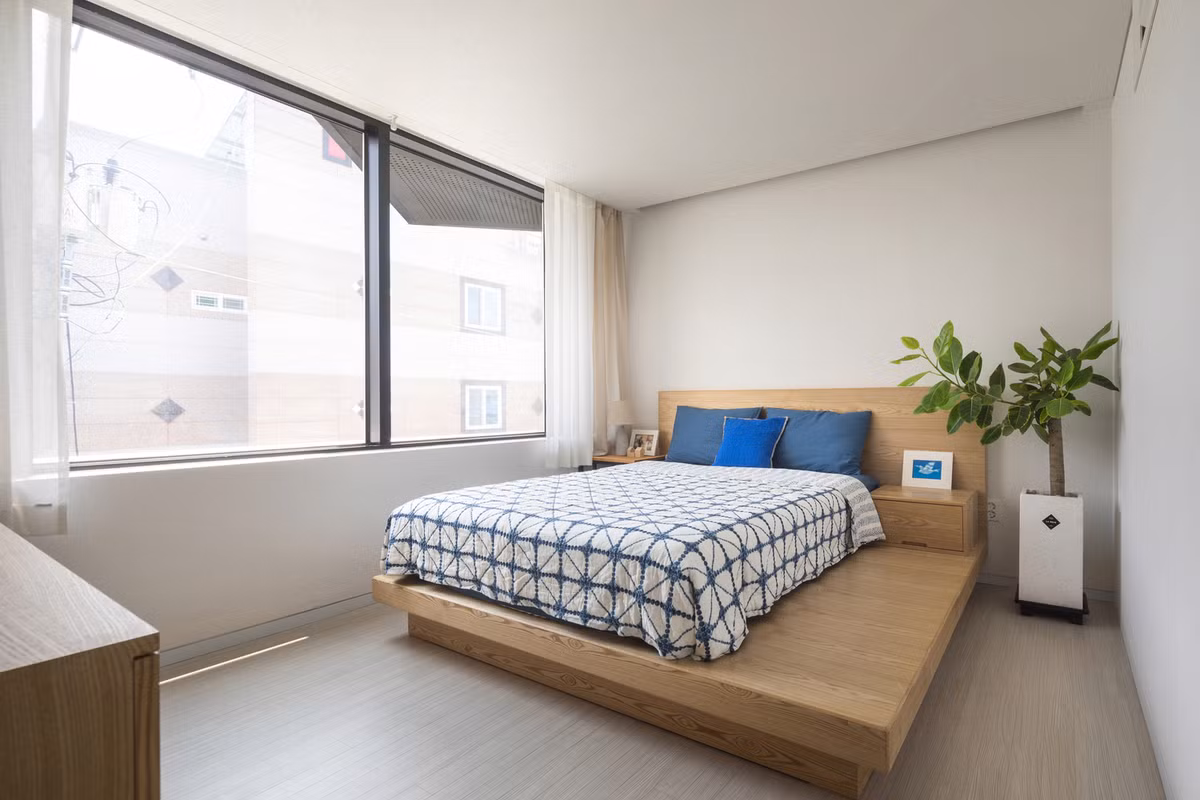 Phòng ngủ với ô cửa sổ lớn để lấy tối đa ánh sáng. Một chậu cây nhỏ đặt ở góc phòng mang lại năng lượng và sự tươi mới cho toàn bộ căn phòng.