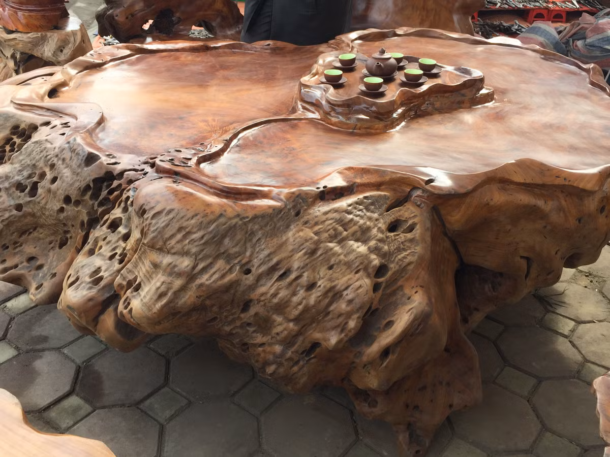 Cận cảnh chiếc bàn cỡ rộng được đẽo từ duy nhất một phiến gỗ. Nghệ nhân vẫn giữ nguyên những chi tiết sần sùi, lỗ chỗ của phiến gỗ để tạo nét tự nhiên vốn có cho chiếc bàn. Đây cũng là điểm chung của các món đồ trong bộ bàn ghế này.