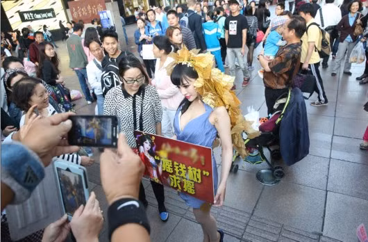 Một người phụ nữ mặc sexy táo bạo đầu đội “lá vàng” ở một con đường ở Thượng Hải, trên tay cầm tấm bảng để tuyên truyền cho trò game mới ra.