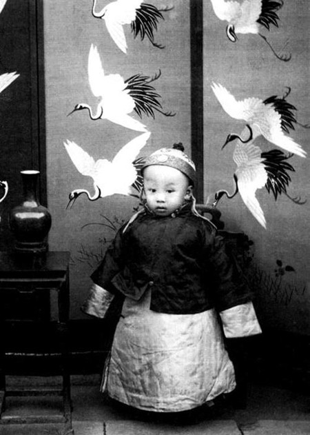 Phổ Nghi - hoàng đế cuối cùng của nhà Thanh trong lịch sử phong kiến Trung Quốc - mặc áo vàng lụa cùng kiểu mũ truyền thống đặc trưng lúc nhỏ.