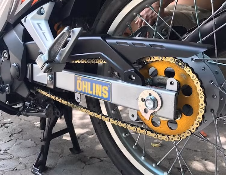 Ở phía sau, chiếc Exciter 135 đã được độ chắn xích từ mẫu xe X1R của Thái Lan, bảo vệ cho bộ nhông sên đĩa SSS vàng óng. Hệ thống phuộc sau monoshock của xe đã được độ lại với cây phuộc RPM và bình dầu rời giấu gọn vào thân xe.