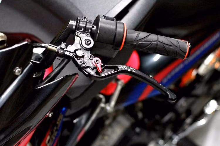 Nằm ở phía trên tay lái của chiếc xe là một số phụ tùng hỗ trợ để đem lại cảm giác lái thoải mái hơn. Trong đó, bên tay phải là bao tay Spider, cùm côn CRG GP2 điều chỉnh tự do cùng cùm công tắc rút gọn so với chiếc Satria nguyên bản.